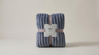 Folded blue-grey ribbed fleece throw blanket on a neutral studio background